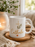 White Catholic Heart Mug with gold Catholic script, leafy cross, and orange heart, staged front view