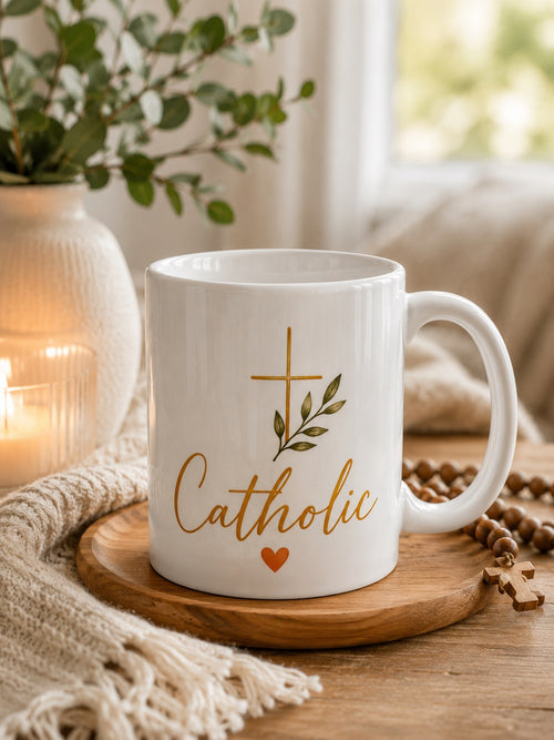 White Catholic Heart Mug with gold Catholic script, leafy cross, and orange heart, staged front view