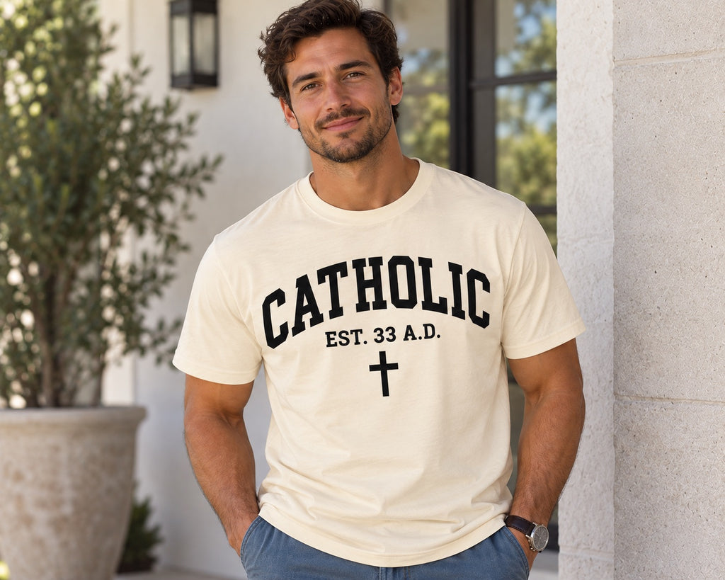 Model wearing a natural Catholic Varsity T-shirt with black lettering, EST. 33 A.D. text, and a cross.