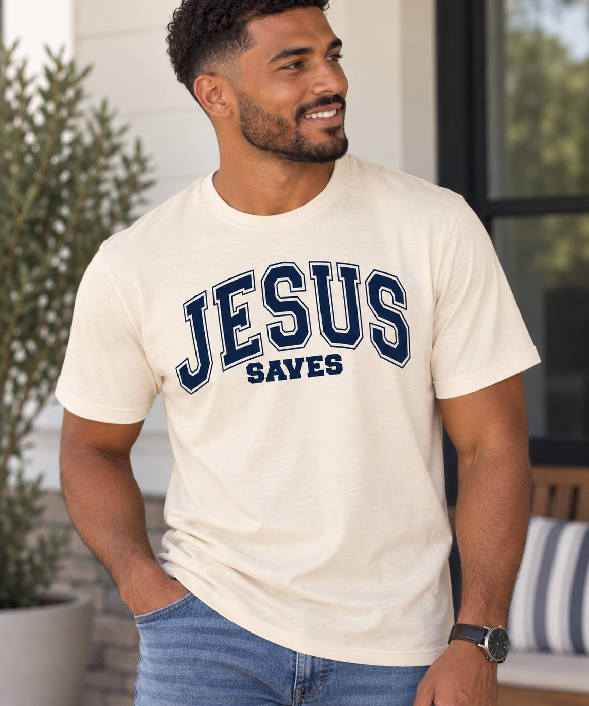 Model wearing a cream Jesus Saves T-shirt with dark blue varsity lettering.
