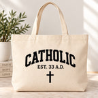 Cream tote bag with black Catholic lettering, EST. 33 A.D. text, and a cross.