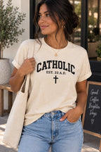 Model wearing a cream T-shirt with black Catholic lettering, EST. 33 A.D. text, and a cross.