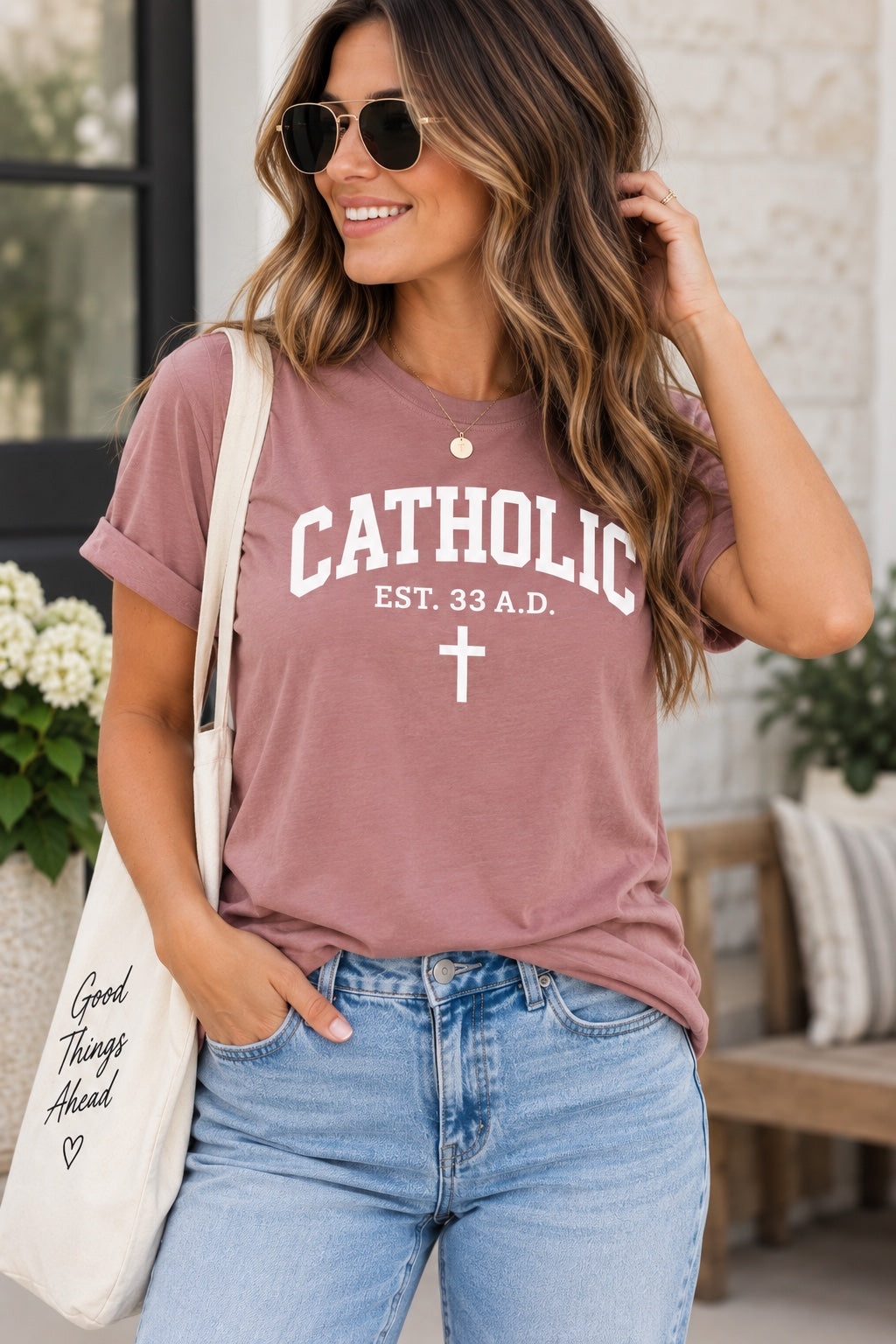 Model wearing a pink T-shirt with white Catholic lettering, EST. 33 A.D. text, and a cross.