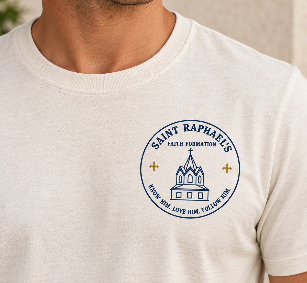 Close-up of the men’s Saint Raphael’s Faith Formation design on the cream T-shirt