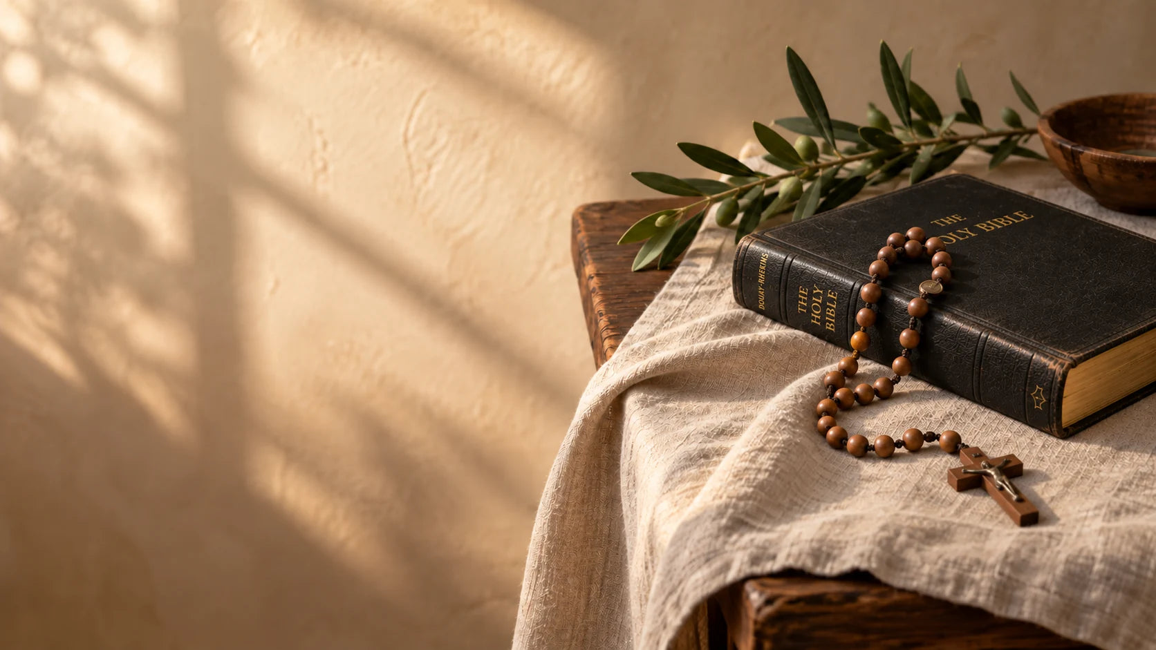 A black Douay-Rheims Bible with a wooden rosary, crucifix, and olive branch