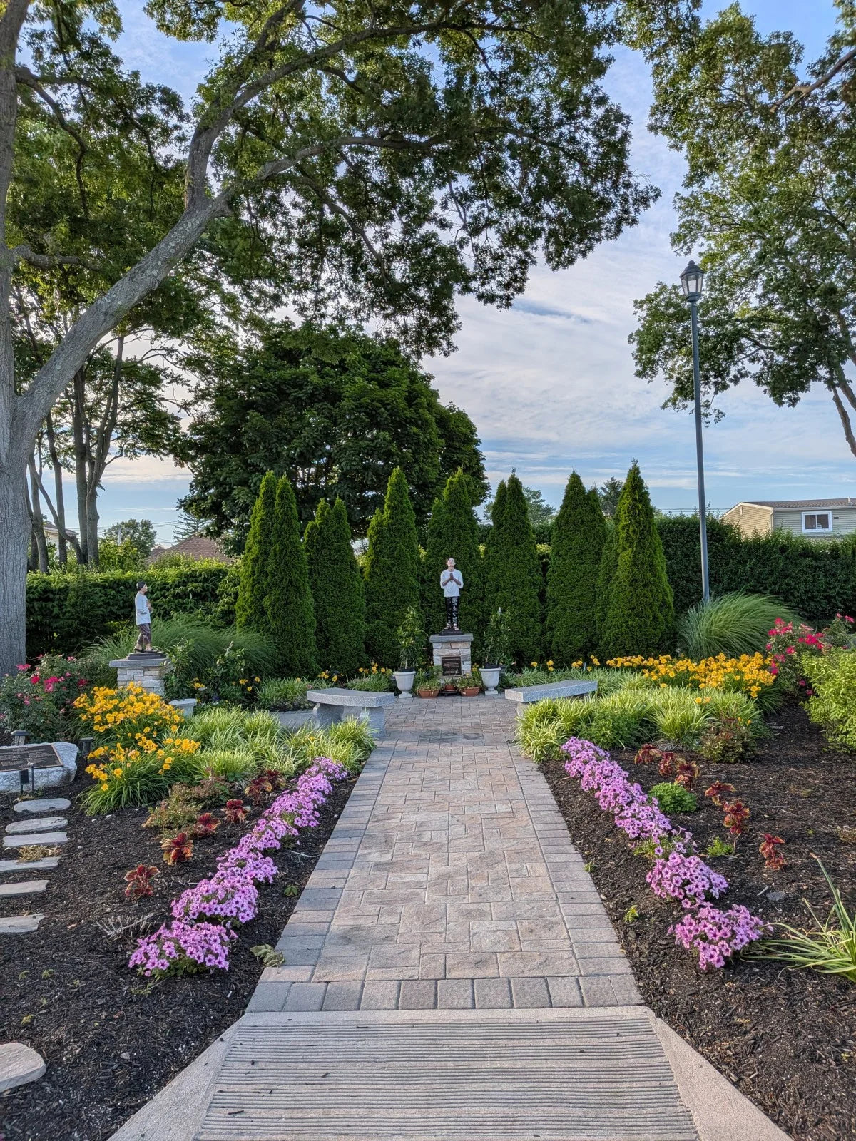 A garden path, flowering beds, benches, and devotional statues in the parish’s San Pedro Garden.